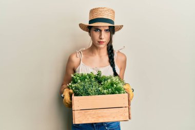 Genç İspanyol kadın elinde yeşil saksı saksısı tutuyor şüpheci ve gergin, sorun yüzünden somurtuyor. negatif kişi. 