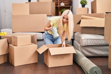 Genç sarışın kadın kahve makinesini açıyor. Yeni evinde yerde oturuyor.