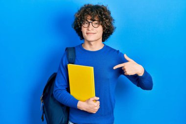 Sırt çantası takan yakışıklı ve elinde kitapla gülümseyen mutlu ve gururlu birini gösteren genç bir adam. 