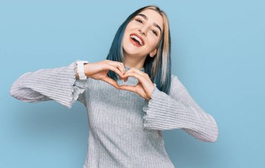 Genç, modern bir kız, sıradan bir süveter giyer, aşka gülümser, elleriyle kalp sembolü çizer. romantik kavram. 