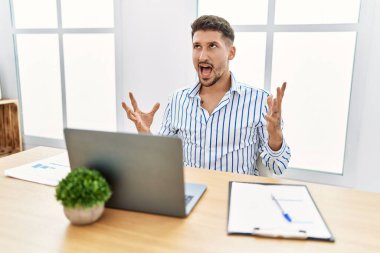 Ofiste çalışan sakallı genç yakışıklı adam bilgisayarını kullanıyor. Deli gibi bağırıyor, bağırıyor ve agresif bir ifade ve kollar havada bağırıyor. hüsran kavramı. 
