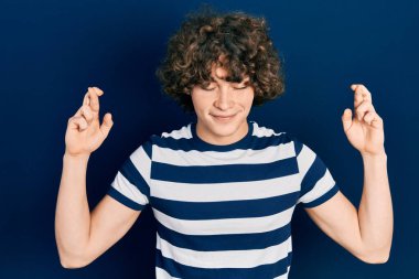 Sıradan çizgili tişört giyen yakışıklı genç adam umut ve gözler kapalı bir şekilde gülümseyerek el işareti yapıyor. Şans ve batıl inançlar. 