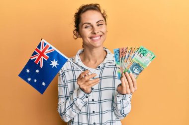 Avustralya bayrağı ve dolarlarla gülümseyen genç esmer kadın yüzünde mutlu ve havalı bir gülümsemeyle. diş gösterme. 