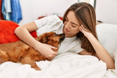Genç İspanyol kadın yatak odasında köpeğe sarılıyor.