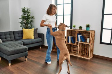 Beyaz bir kadın gülümseyerek evde köpekle dans ediyor.