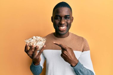 Genç Afrikalı Amerikalı adam elinde kabak tohumlarıyla kaseyle gülümsüyor. 