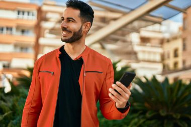 Genç İspanyol adam şehirde akıllı telefon kullanarak mutlu gülümsüyor..
