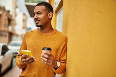 Genç Afrikalı Amerikalı adam akıllı telefon kullanıyor. Şehirde kahve içiyor..