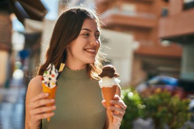Genç beyaz kız gülümseyerek şehirde dondurma yiyor..