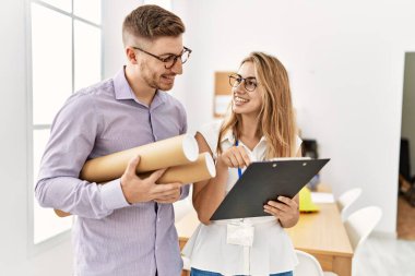 Mimarlık stüdyosunda elinde planlar ve pano tutarak mutlu gülümseyen iki genç mimar..