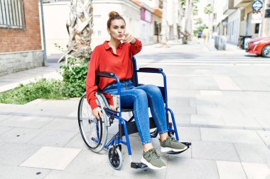 Tekerlekli sandalyede oturan genç esmer kadın kamerayı işaret ediyor ve sen kendinden emin bir şekilde ciddi görünüyorsun. 