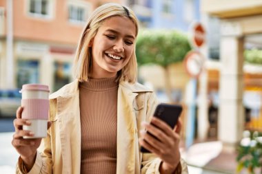Genç sarışın kız şehirde kahve içerken akıllı telefon kullanıyor..