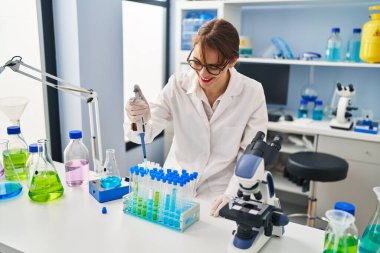 Genç beyaz kadın bilim adamı üniforması giyiyor. Laboratuvarda pipet kullanıyor.