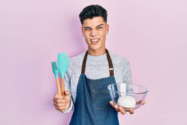 Genç İspanyol adam ekmek hamuru tutuyor ve yemek aletleri habersiz ve kafası karışık bir ifade sergiliyor. şüphe kavramı. 