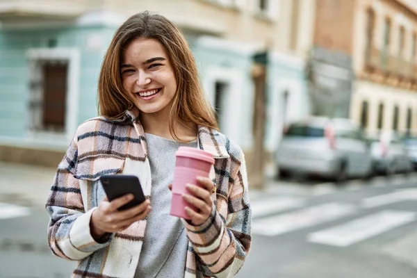 Genç Sarışın Kadın Gülümsüyor Akıllı Telefon Kullanıyor Sokakta Kahve Tutuyor — Stok fotoğraf