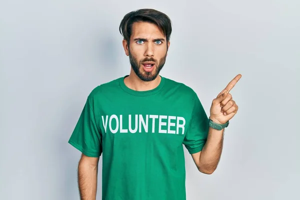 Jovem Hispânico Vestindo Camiseta Voluntária Surpreso Apontando Com Dedo Para — Fotografia de Stock