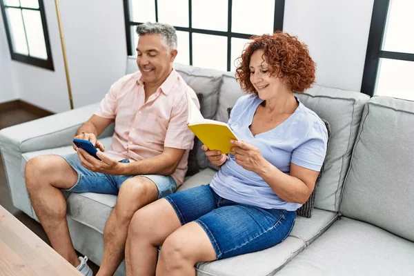 Middle Age Man Woman Couple Using Smartphone Reading Book Sitting — Φωτογραφία Αρχείου