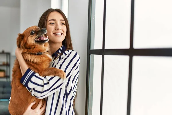 Genç Spanyol Kadın Gülümsüyor Kendine Güvenen Sarılan Köpek Evde Duruyor — Stok fotoğraf