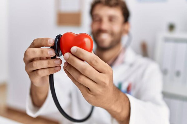Young hispanic man wearing doctor uniform examining heart at clinic