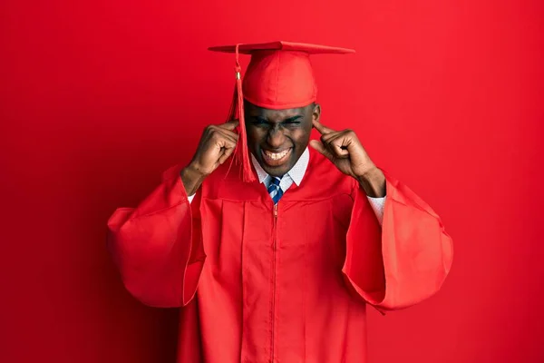 年轻的非洲裔美国人 戴着毕业典礼帽 身穿礼袍 用手指捂住耳朵 对嘈杂的音乐感到恼怒 聋人概念 — 图库照片