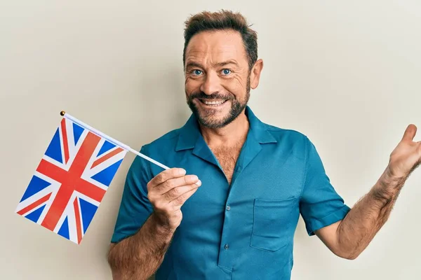 Middle age man holding united kingdom flag celebrating achievement with happy smile and winner expression with raised hand