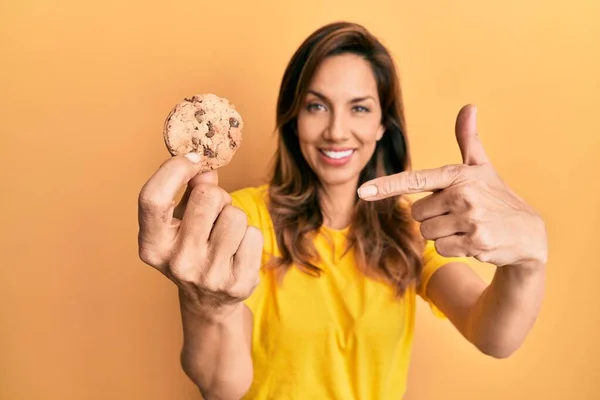 Jovem Latina Segurando Biscoito Sorrindo Feliz Apontando Com Mão Dedo — Fotografia de Stock