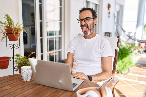 自宅でコンピュータのラップトップを使用している中年の男性が面白い表情で幸せ舌を突き出しています 感情の概念 — ストック写真