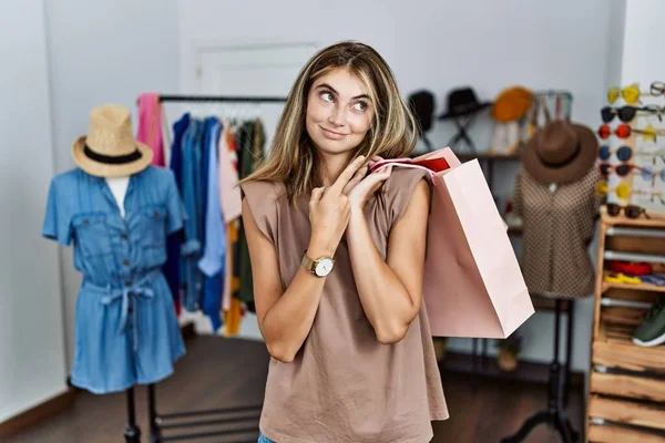 年轻的金发女子拿着购物袋站在零售店 手指头指向广告的侧面 严肃而沉着 — 图库照片