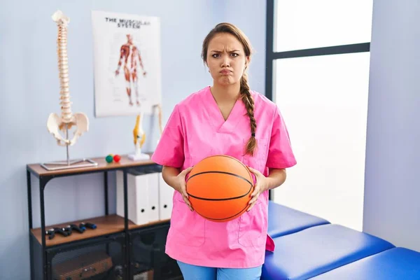 バスケットボールの懐疑的で神経を保持する理学療法クリニックで働く若いヒスパニック系の女性は 問題のために動揺を眉をひそめて 否定的な人 — ストック写真