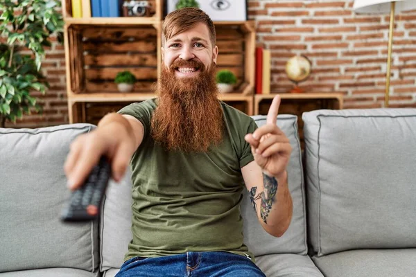 長いです髭を生やした男持っていますテレビリモコン笑顔幸せなポインティングとともに手と指で側面 — ストック写真