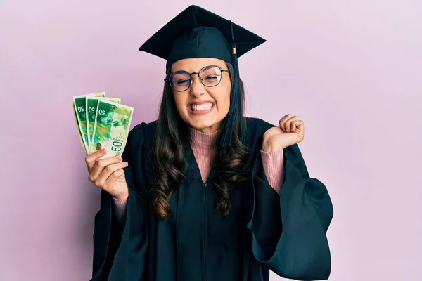 Young Hispanic Woman Wearing Graduation Uniform Holding Israel Shekels Banknotes — Stock Photo, Image