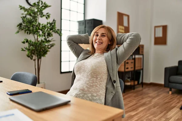 Middle age businesswoman smiling happy relaxed with hands on head at the office.