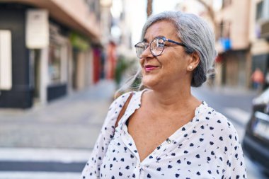 Orta yaşlı bir kadın sokakta kendine güvenerek gülümsüyor.