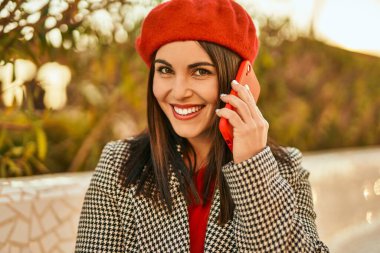 Genç İspanyol kadın gülümsüyor. Parktaki akıllı telefondan konuşarak mutlu oluyor..