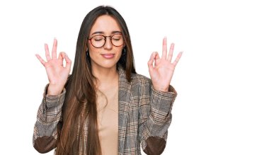 İş kıyafetleri giymiş, gözlüklü, gülümseyen, gözleri kapalı meditasyon yaparken parmaklarıyla gülümseyen İspanyol bir kız. yoga konsepti. 
