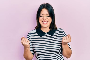 Gündelik kıyafetler giyen genç İspanyol kadın başarı için heyecanlı kolları havada ve gözleri kapalı zaferi kutlarken gülümsüyor. Kazanan konsept. 