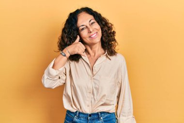 Orta yaşlı İspanyol kadın, günlük kıyafetler giyip gülümsüyor telefonla el ve parmak hareketleri yapıyor telefonda konuşuyor gibi. iletişim kavramları. 