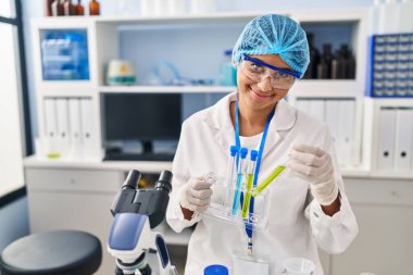 Laboratuvarda deney tüpü tutan bilim adamı üniforması giyen genç Latin kadın.