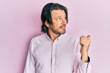 Orta yaşlı, iş gömleği giyen, gülümseyen, gülen yüzlü ve baş parmağıyla yan tarafı gösteren yakışıklı bir adam.. 