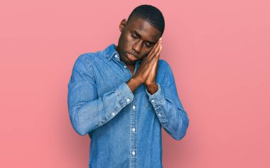 Genç Afro-Amerikan adam günlük kıyafetler giyip uyuyordu. Yorgundu. Hayal kuruyordu ve elleriyle poz veriyordu.. 