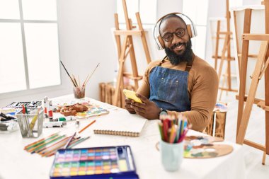 Genç Afrikalı Amerikalı sanatçı sanat stüdyosunda kulaklık ve akıllı telefon kullanıyor..