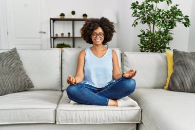 Genç Afrikalı Amerikalı kadın evdeki kanepede yoga yapıyor.