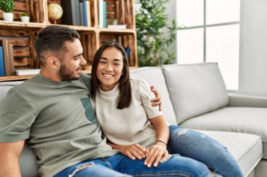 Kanepede oturan genç latin çift evde sarılıyorlar..