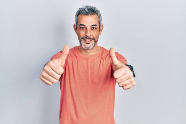 Gri tişörtlü yakışıklı, orta yaşlı bir adam. Elle olumlu jest yapmayı onaylıyor. Gülümsüyor ve başarı için seviniyor. kazanan jest. 