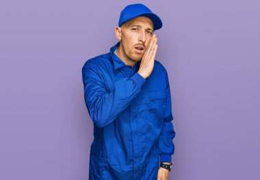 Kel, sakallı, inşaatçı tulumu giyen, elleri ağızda gizli dedikodular fısıldayan, kötü niyetli konuşmalar fısıldayan bir adam. 