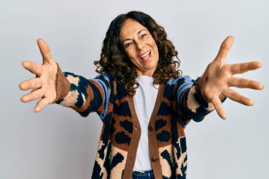 Orta yaşlı İspanyol kadın sıradan kıyafetler giyip kameraya bakıyor. Sarılmak için kollarını açmış gülümsüyor. Mutluluğu kucaklayan neşeli bir ifade.. 