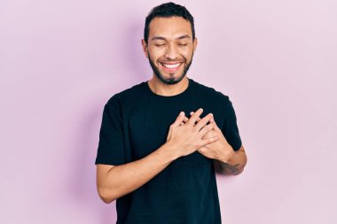 Sakallı, sıradan siyah tişörtlü, elleri göğsünde, gözleri kapalı, yüzünde minnet ifadesi olan İspanyol bir adam. sağlık kavramı. 