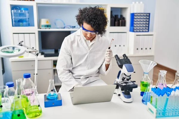 Young Hispanic Man Wearing Scientist Uniform Using Laptop Analysing Blood — стоковое фото