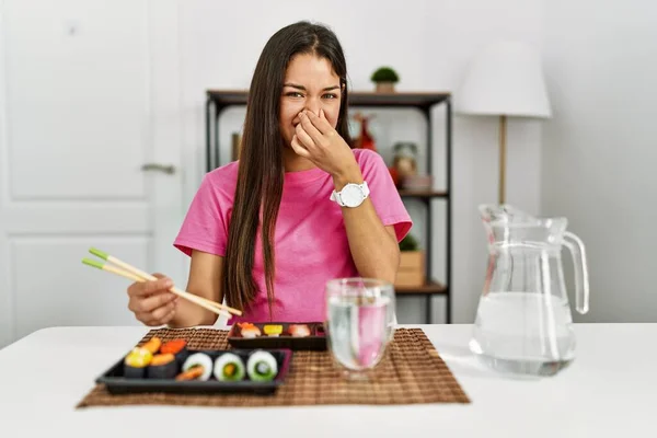 若いブルネットの女性は 鼻の上に指で息を保持し 何か臭くて嫌な 耐え難い匂いを嗅ぐ箸を使用して寿司を食べる 臭いが悪い — ストック写真