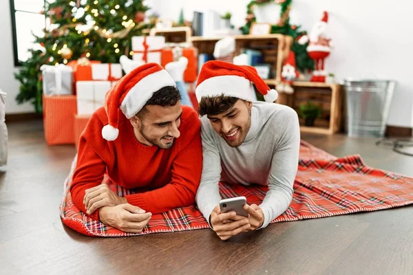 Dva Hispánští Muži Pár Pomocí Smartphone Ležící Vánočního Stromku Doma — Stock fotografie